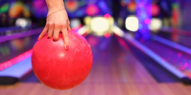 Main tenant une boule de bowling face à une piste