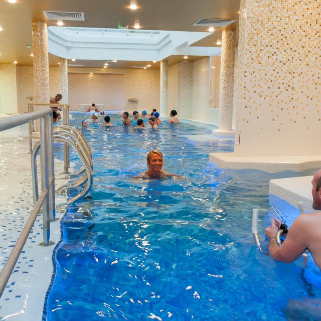 Femme dans le bassin du Spa des Thermes de Contrexéville avec un groupe dans le fond faisant du sport dans l'eau