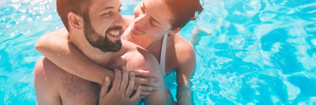 Cheerful youthful guy and lady resting while swimming pool outdoor. Couple in water.
