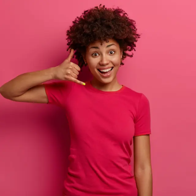 Jeune femme souriante mimant un appel téléphonique avec sa main droite