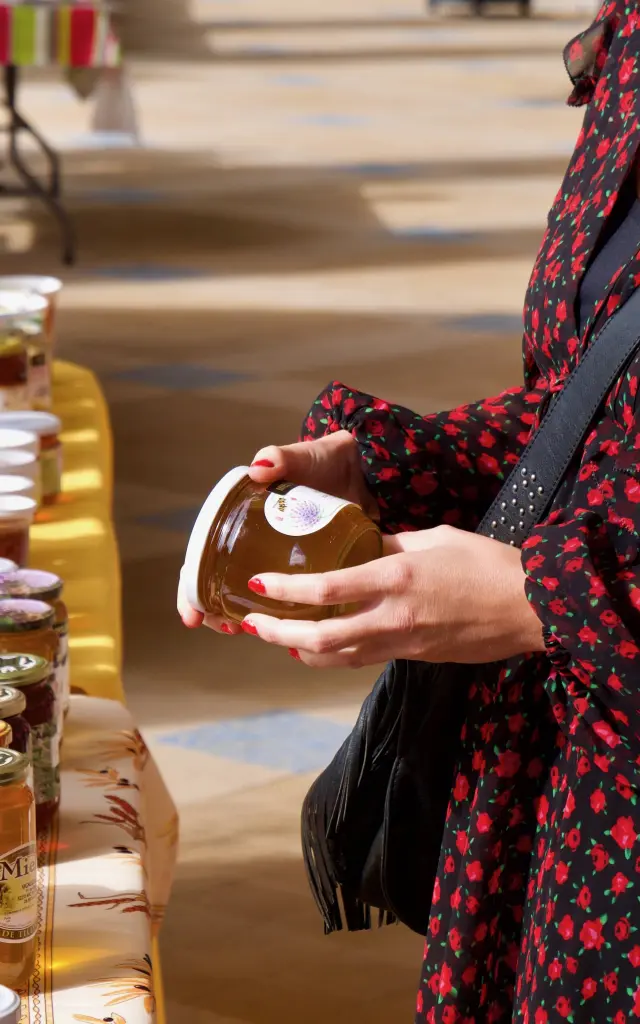 Jeune femme tenant un pot de miel lors d'un marché du terroir sous la galerie thermale de Contrexéville